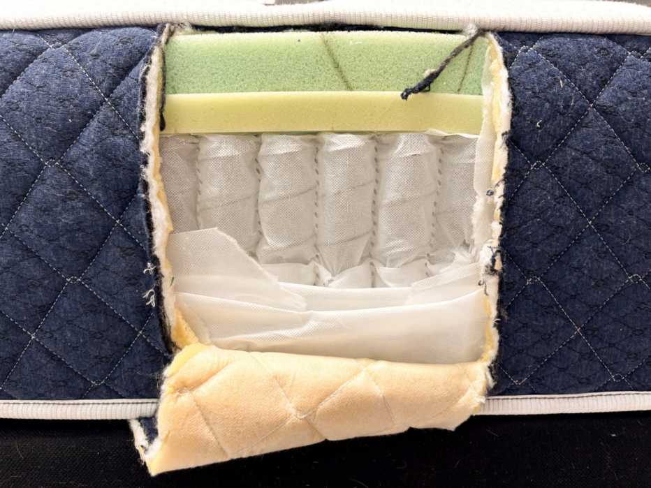 The side of a mattress is cut open, revealing an interior of pocketed coils beneath two layers of memory foam