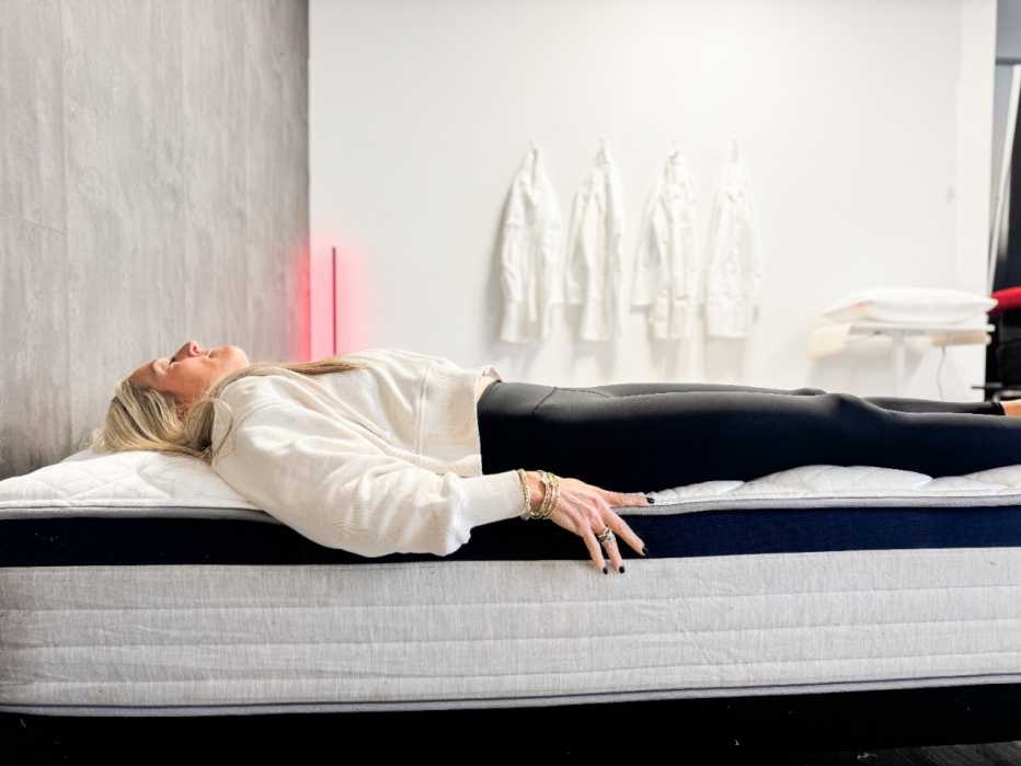 Woman lies on her back on the edge of a mattress
