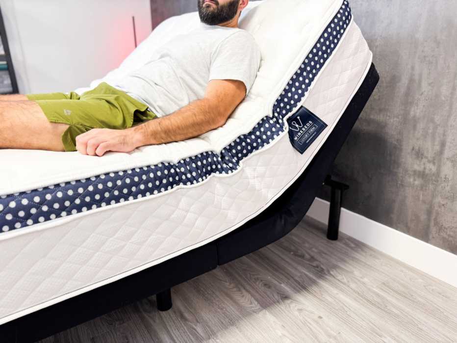 A man sitting on the WinkBed mattress while it’s on an adjustable base.
