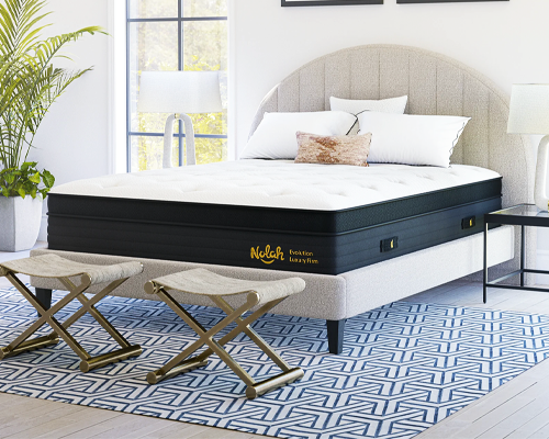 The Nolah Evolution mattress in a white bedroom with a plant in the corner.
