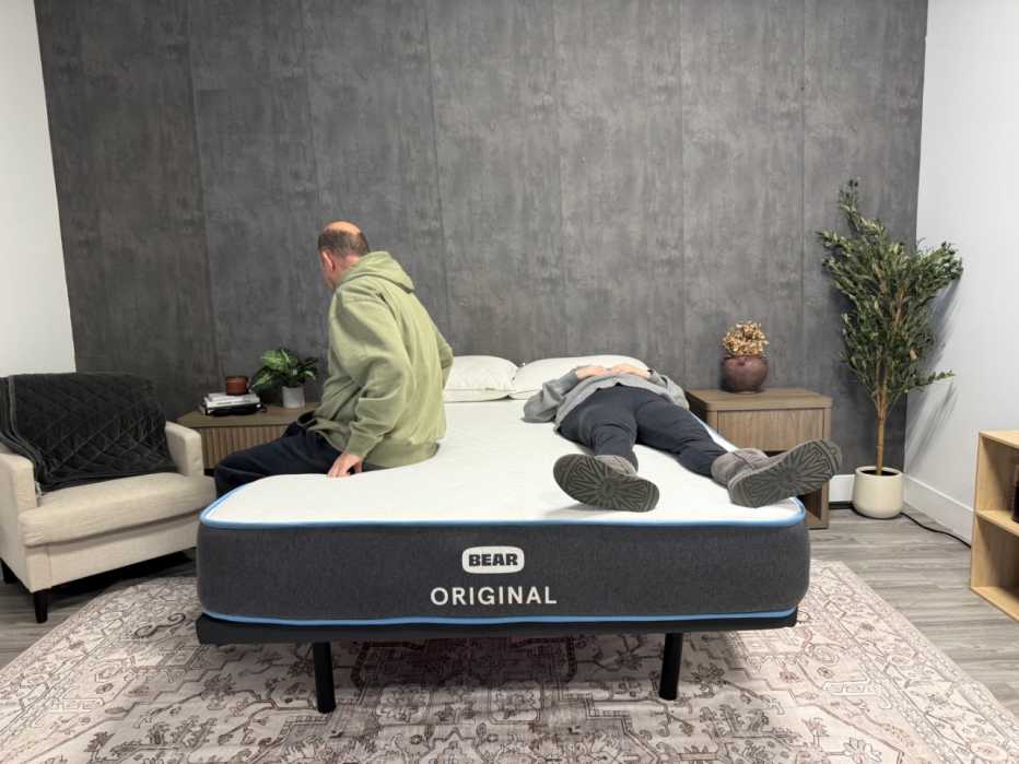 Man sitting on the edge of a bed while a woman lies on her back on the opposite side