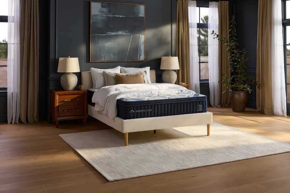 The DreamCloud Premier mattress in a dark blue bedroom with long curtains. 
