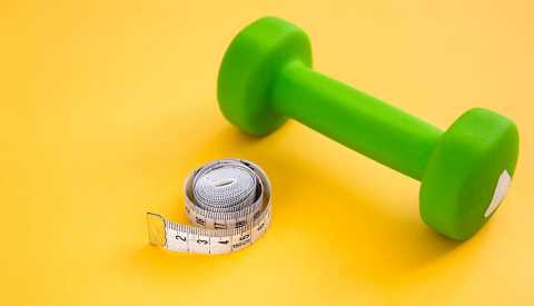 dumbbell and measuring tape on a yellow background dumbbell and measuring tape on a yellow background