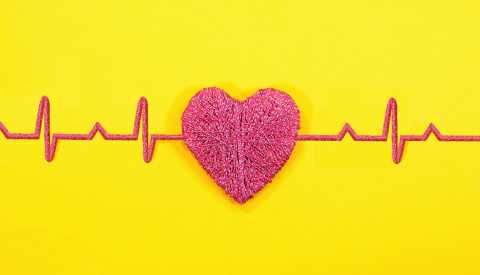 a red heart made of yarn shows a heart beat reading of a normal heart rate on a bright yellow background