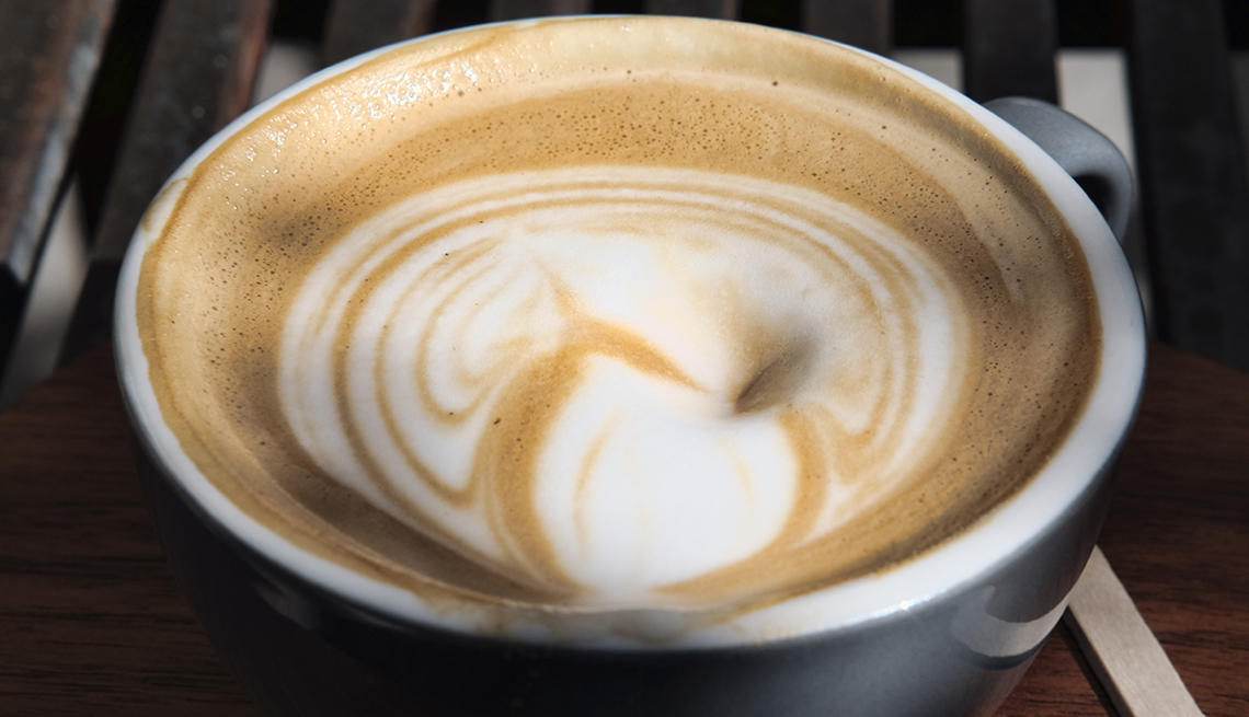 A white coffee mug containing coffee with white cream mixed in.