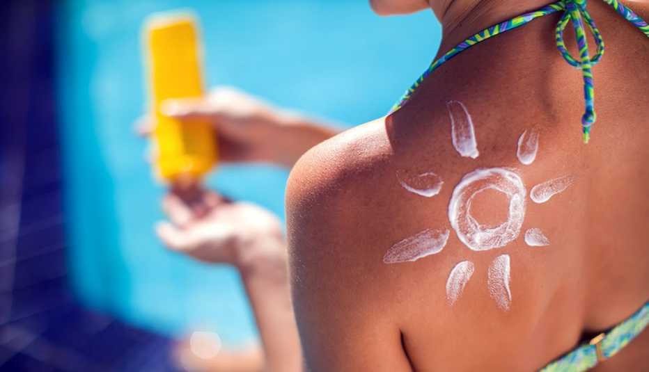 woman with sun protection cream on her back in shape of sun sitting on the pool