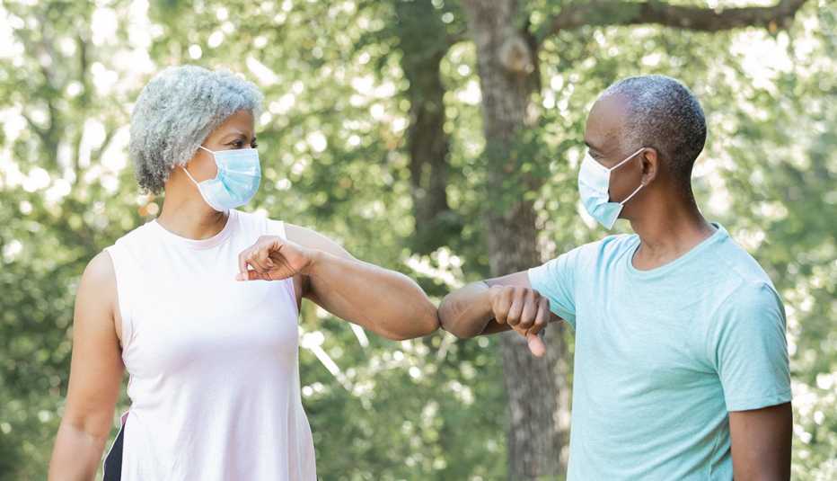 Man and woman wearing masks greet each other by touching elbows Man and woman wearing masks greet each other by touching elbows