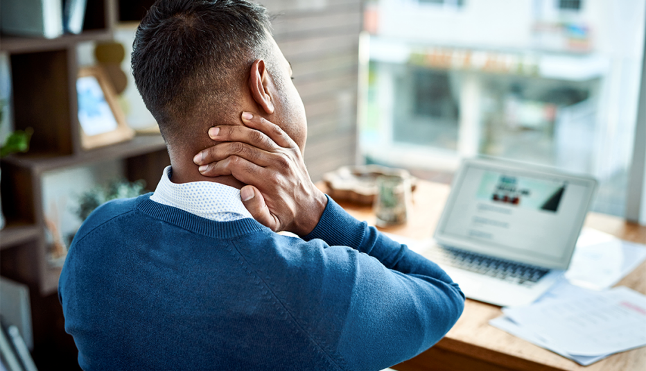 A man rubbing his neck pain as he works at a desk A man rubbing his neck pain as he works at a desk