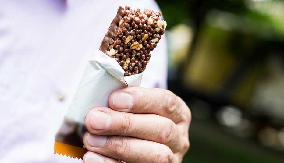 close up of a man in a purple shirt holding a half-eaten protein bar full of hidden sugar and excess calories