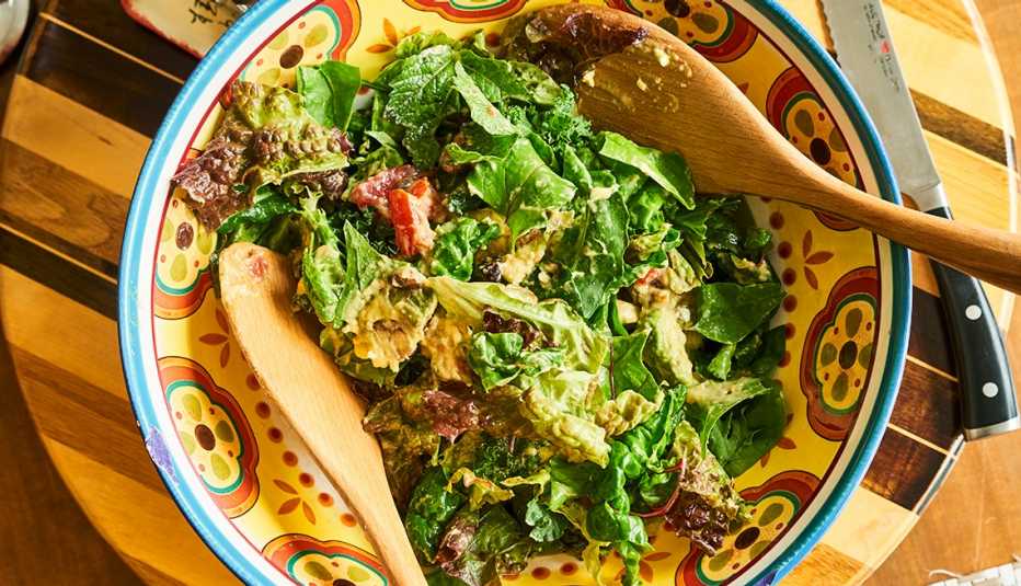 Salad sitting in a brightly-colored bowl, wooden tongs sitting in the bowl.