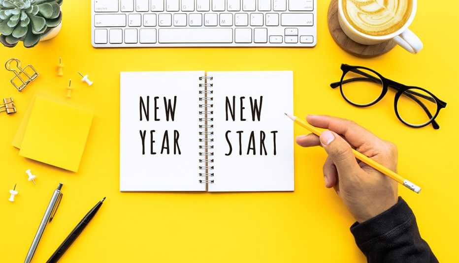 photograph of a man holding a pencil with 'New Year New Start' written in an open notebook surrounded by pens, glasses and other office supplies on a yellow background representing the importance of healthy new year's resolutions