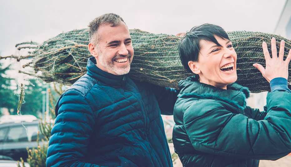 Happy couple carrying Christmas tree on their shoulders