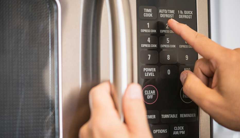 Close up of a man punching the time in on a microwave.
