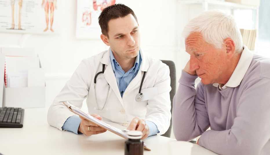 A man appears unhappy with his hand to his face during a visit with his doctor