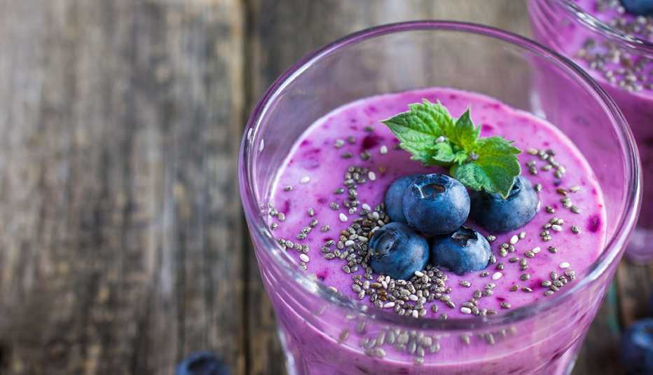 close up of a mixed berry smoothie for healthy weight gain with blueberries, chia seeds, and a sprig of mint on top set on a kitchen table
