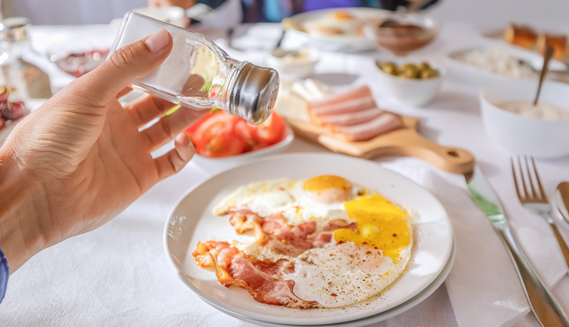 adding salt to a bacon and egg breakfast