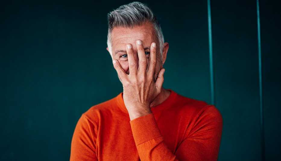 man covering face with hand in front of wall man covering face with hand in front of wall