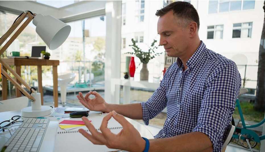 Mature man sitting at his desk at work meditating.