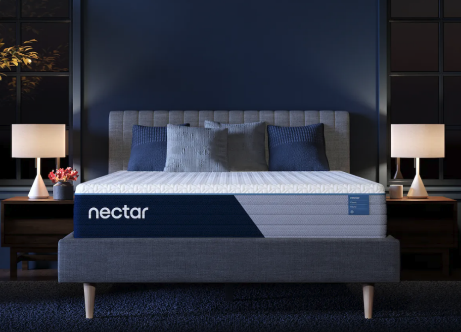 The Nectar Classic Memory Foam mattress in a dim bedroom display with two lamps.