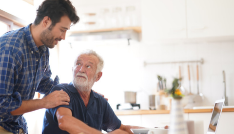 a man sitting at a kitchen table eating while another man stands behind him