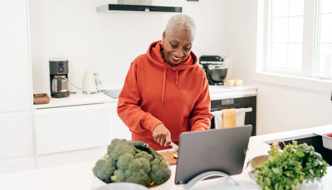 a woman chopping vegetables in her kitchen while looking at a tablet