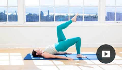 Pilates instructor Erin Wilson in a modified plank pose on a mat in a studio with a window looking out onto the water, with video player icon in right corner