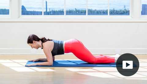 Pilates instructor Erin Wilson in a modified plank pose on a mat in a studio with a window looking out onto the water, with video icon overlay