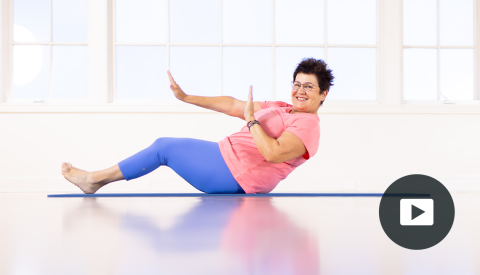 karen sanzo sitting on mat, leaning back, right hand pushing forward, left arm bent; picture of play button in bottom right corner