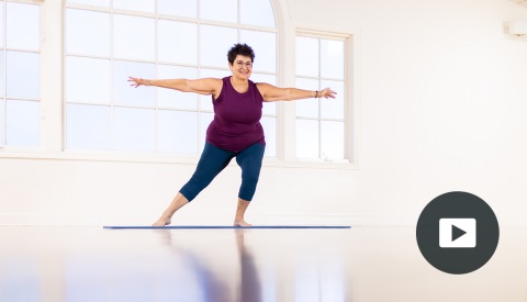 karen sanzo standing on mat with arms straight out to the side, left leg slightly bent, right leg stretched out with toes touching mat; picture of play button on bottom right corner