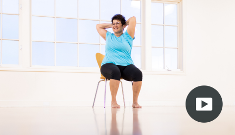 karen sanzo sitting in chair, twisting body, hands behind head; picture of play button on bottom right corner