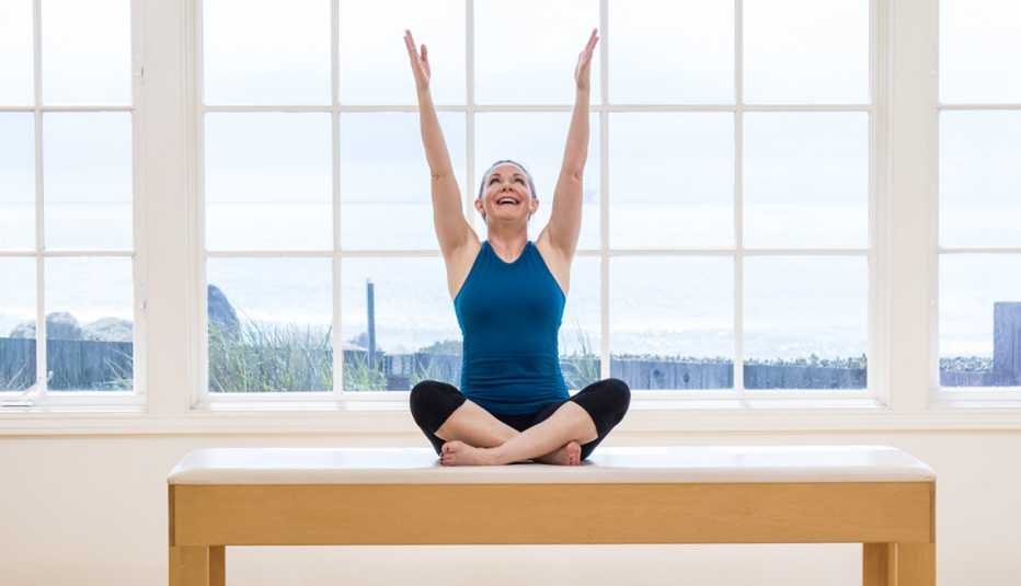 woman doing Pilates, arms raised and legs crossed, on a table in front of a window woman doing Pilates, arms raised and legs crossed, on a table in front of a window