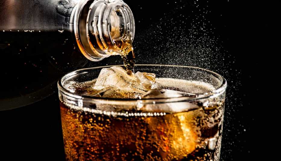 Soda being poured into a glass with ice