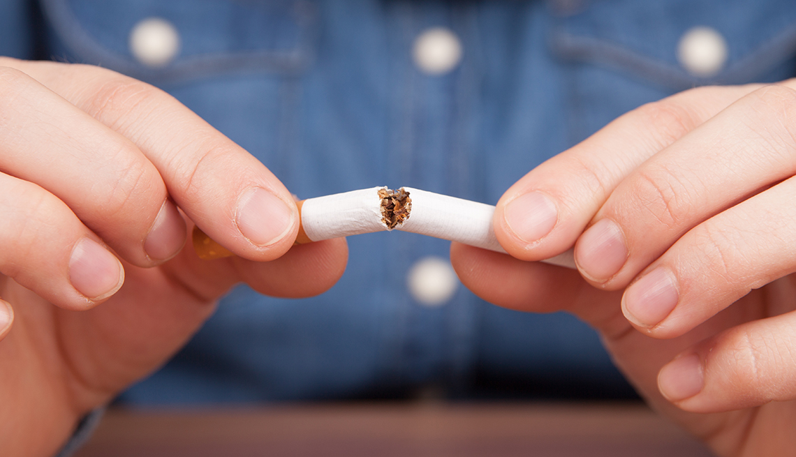 Close-up of a man's hands breaking a cigarette in half. His blue shirt in the background.