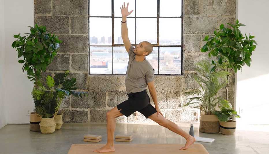 brandon dawson-jarvis on mat in front lunge with right arm raised in air; window behind him, tall plants on sides of window