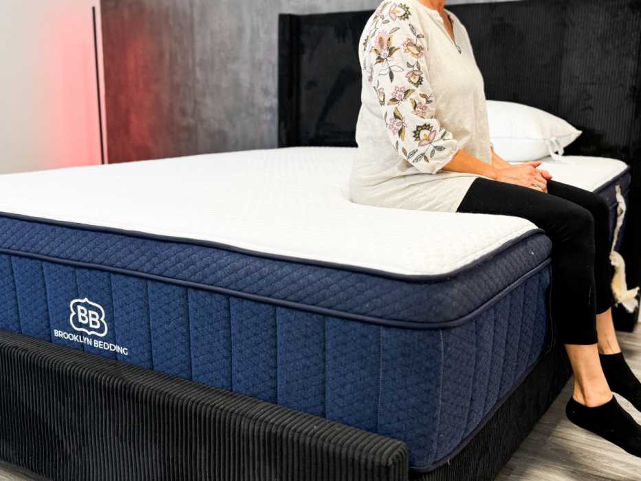  A woman sitting on the edge of the Brooklyn Bedding Aurora Luxe mattress.