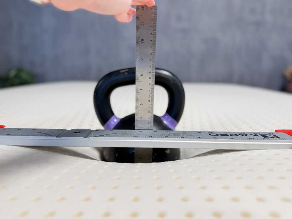  A kettlebell weight sinking into a mattress topper with a ruler measuring its depth
