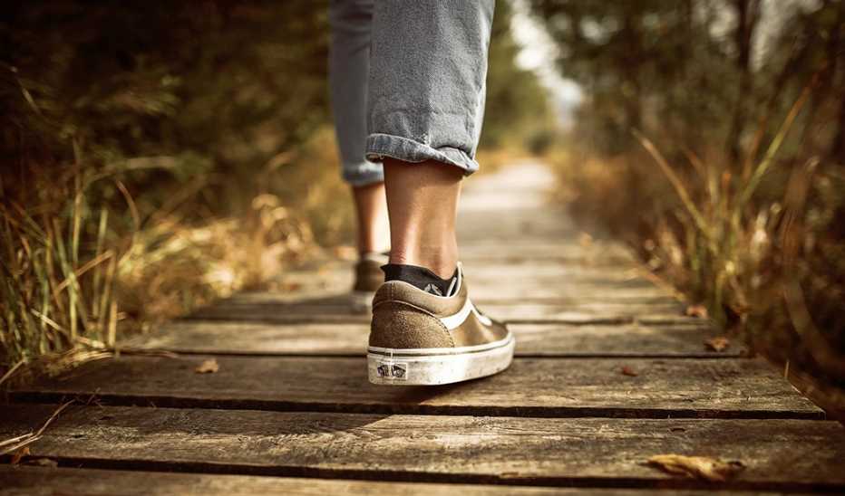 A close up of the shoes of a person walking on a wooden path