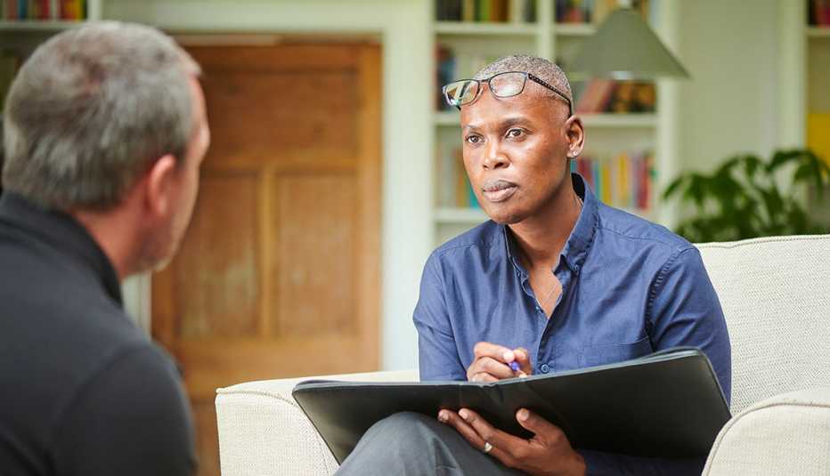 a female cognitive behavioral therapist holding a black folder and a pen listens to her male patient