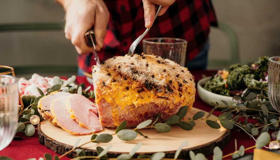 man slices a holiday ham on a set dinner table