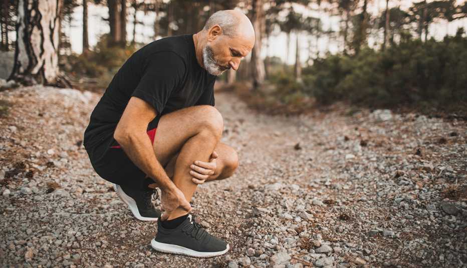 a man kneeling in a forest holding his ankle injured due to a stress fracture