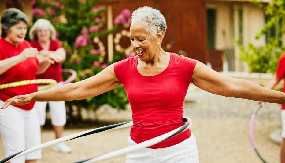 a woman in a red shirt practicing hula hooping with her outdoor fitness class to be more active and make fitness fun and playful 