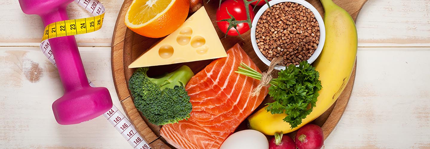 Dumbbell, tape measure next to plate of high-protein food, vegetables and fruit on wooden table