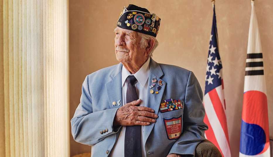 Sal Scarlato at his New York home. Sal Scarlato places his hand on his chest. American and Korean flags are in the background.
