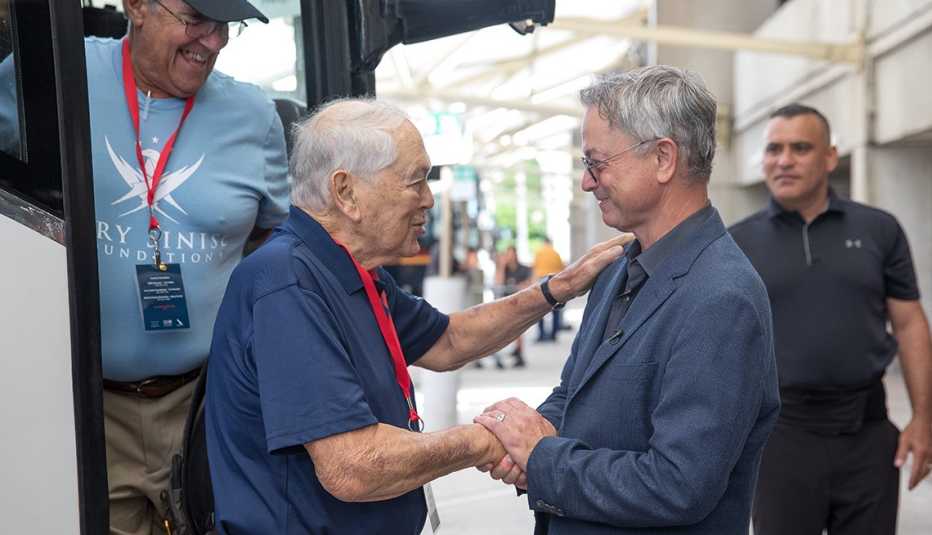 two men shake hands in front of a charter bus.