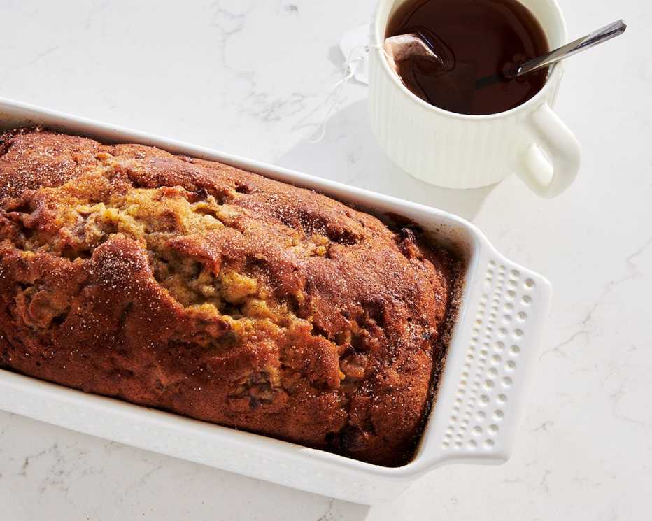 banana bread rests in a white baking dish next to tea in a white cup
