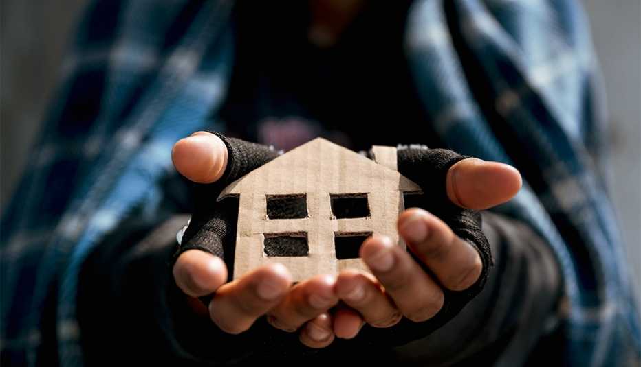 homeless man holds a house made of brown cardboard