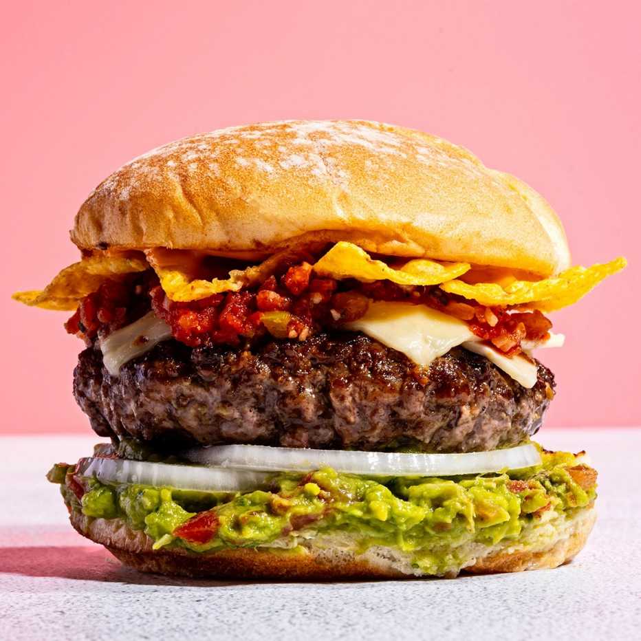 A hamburger with guacamole, onion, chips, cheese and other toppings