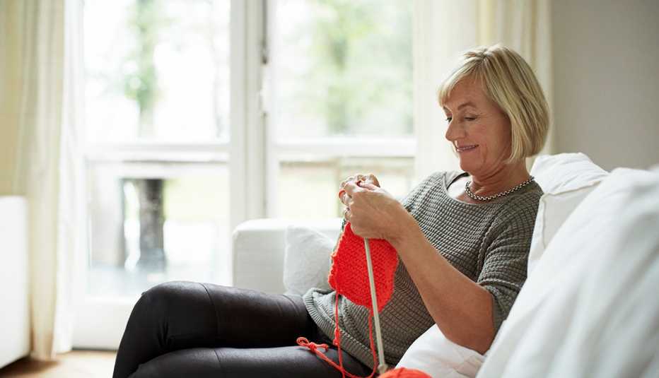 Senior woman knitting while sitting on sofa in house