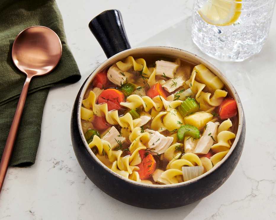 a bowl of chicken noodle soup on a white table