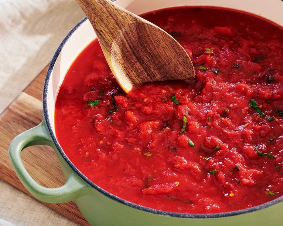 a wooden spoon stirs red sauce in a green pot